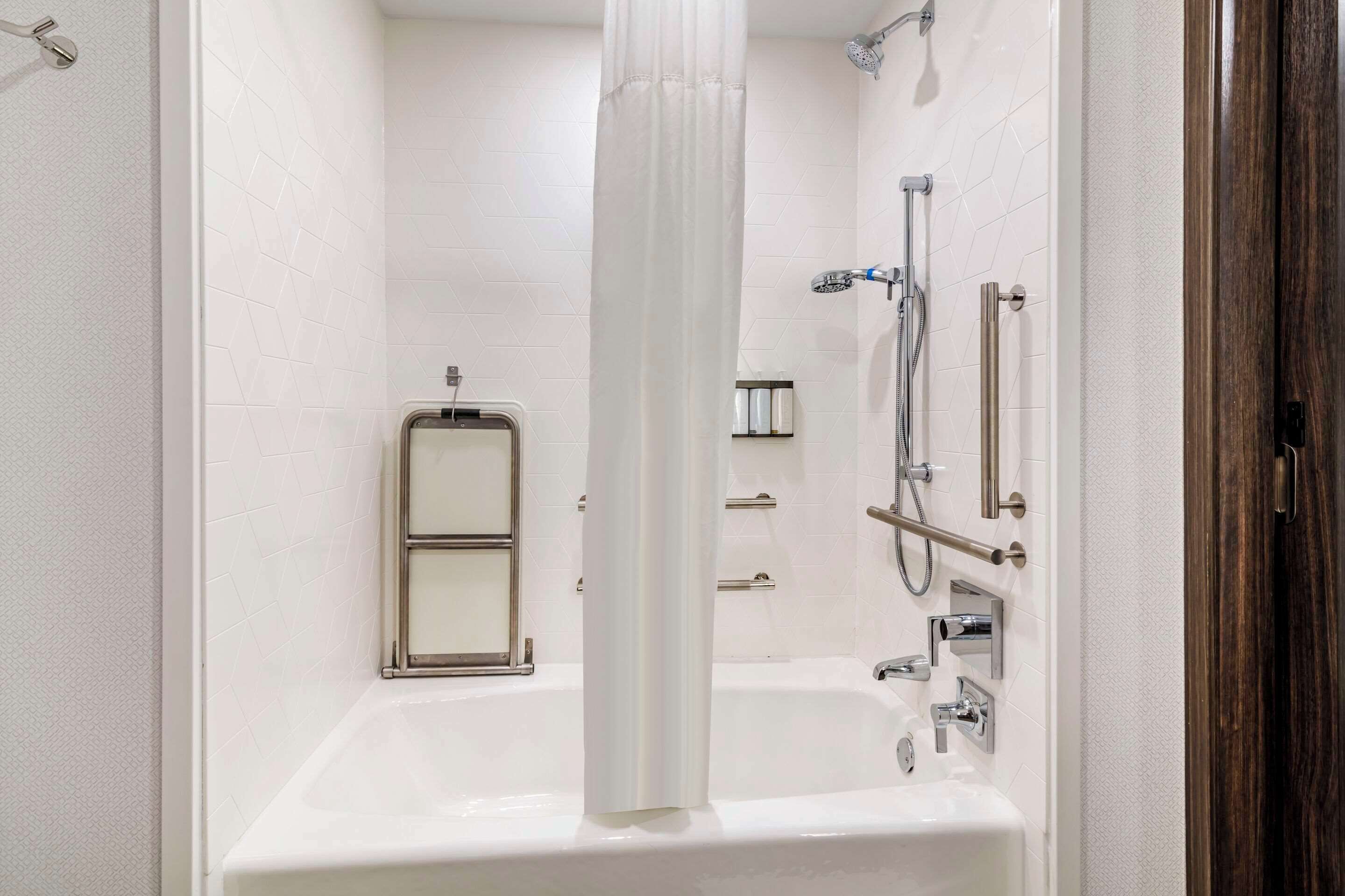 Un baño moderno con una bañera blanca, una ducha con cabezal de ducha manual y un inodoro con mampara de vidrio.
