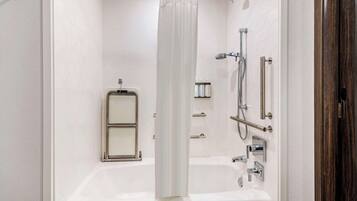 Un baño moderno con una bañera blanca, una ducha con cabezal de ducha manual y un inodoro con mampara de vidrio.