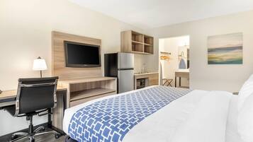 Ein Hotelzimmer mit Bett, Schreibtisch mit Computer, Fernseher, Kühlschrank und einer Küchenzeile.