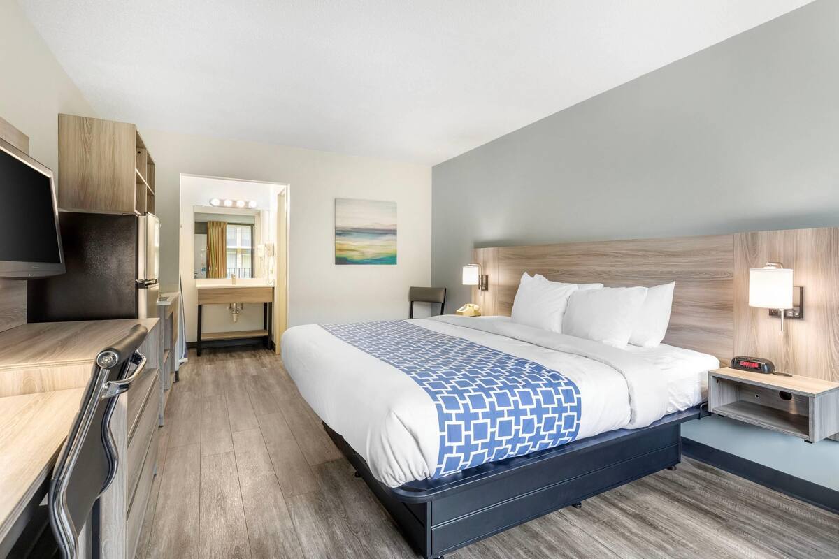 A hotel room with a bed, bedside tables, a TV, a desk, and a mirror.