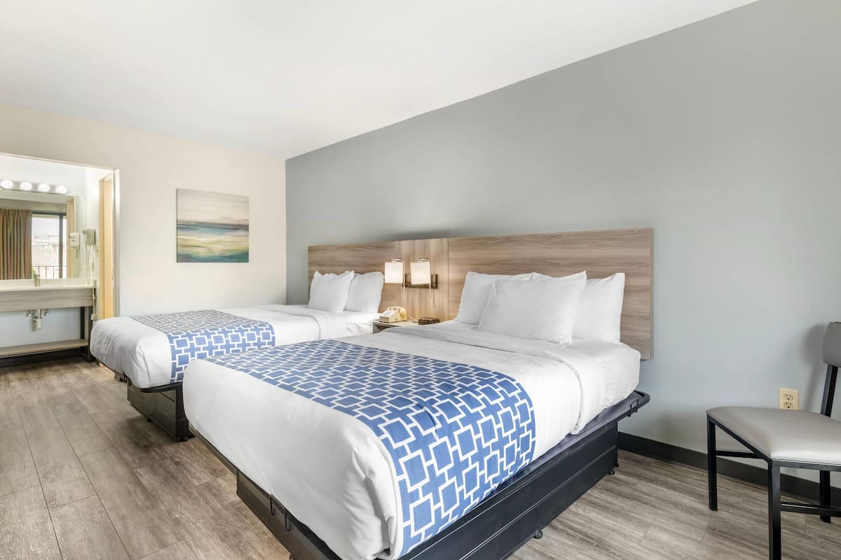 A hotel room with two beds, a large mirror, a painting, and a chair.