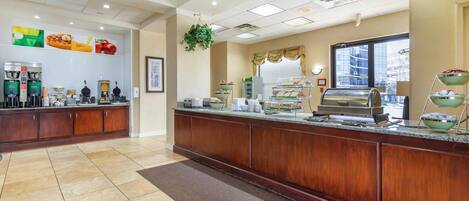 A hotel reception area with a wooden counter, coffee machines, and a buffet display.
