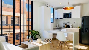 A modern kitchen with white cabinets, a black refrigerator, and a microwave. There is a dining area with a white table and chairs.