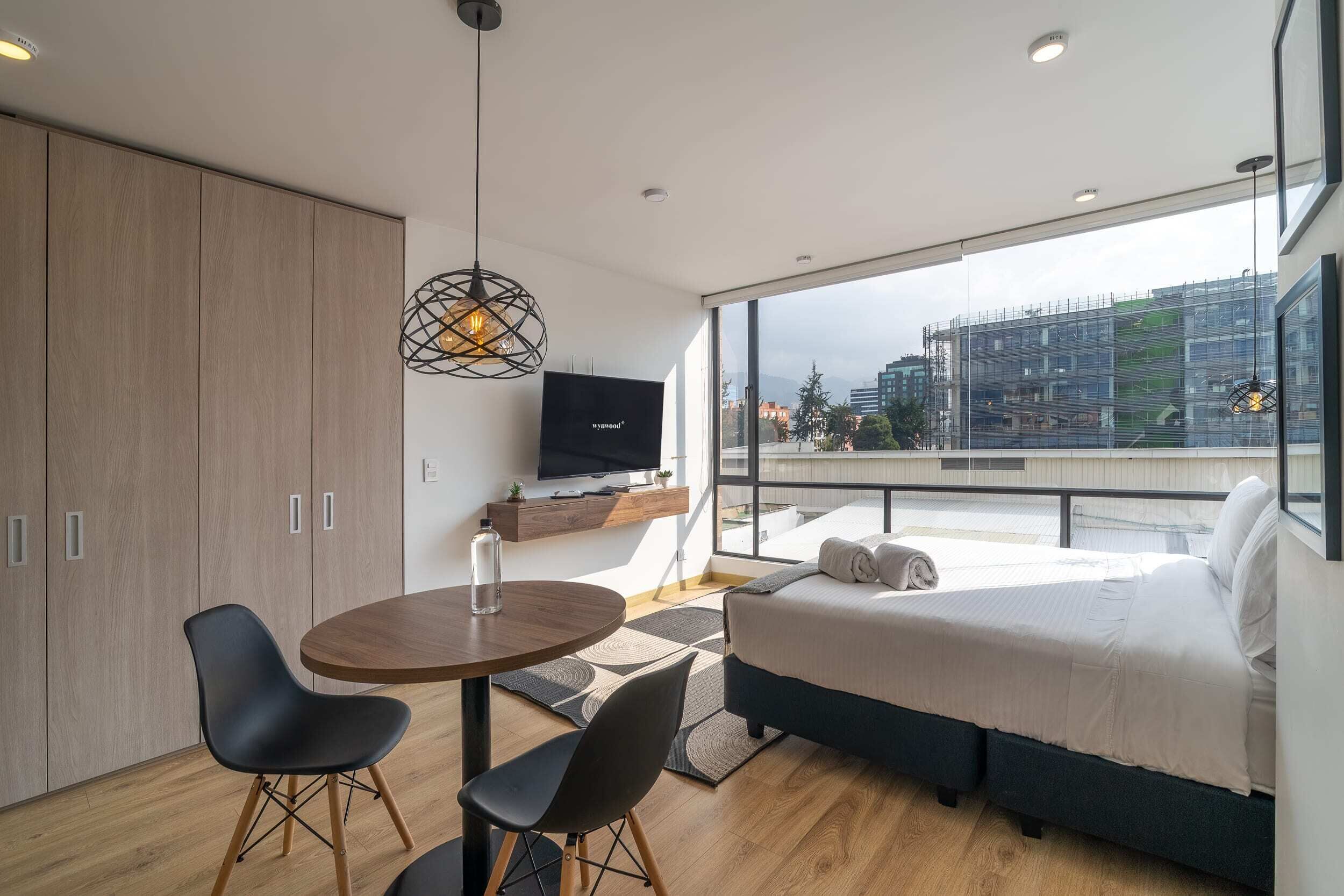 Een moderne slaapkamer met een bed, een televisie en een zithoek met stoelen en een tafel.