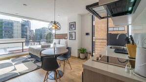 A modern apartment with a balcony, a dining area, a kitchen, and a large window offering a city view.