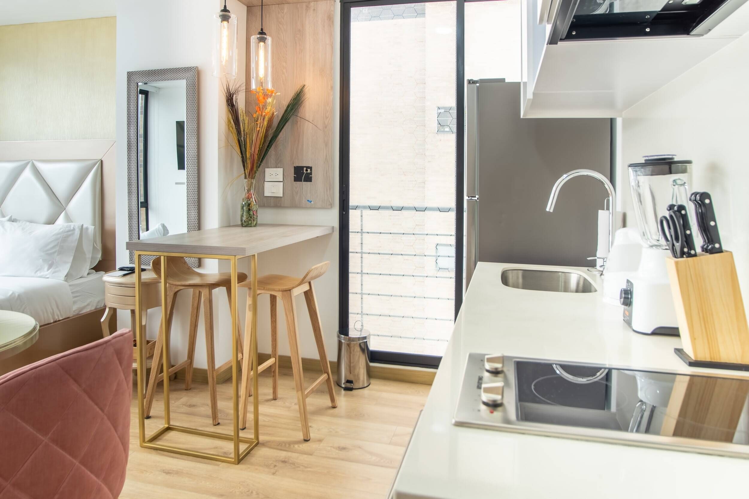 Ein modernes Hotelzimmer mit einem Bett, einem kleinen Schreibtisch mit Stuhl, einer Küchenzeile mit Spüle und Kühlschrank sowie einem Balkon mit Aussicht.