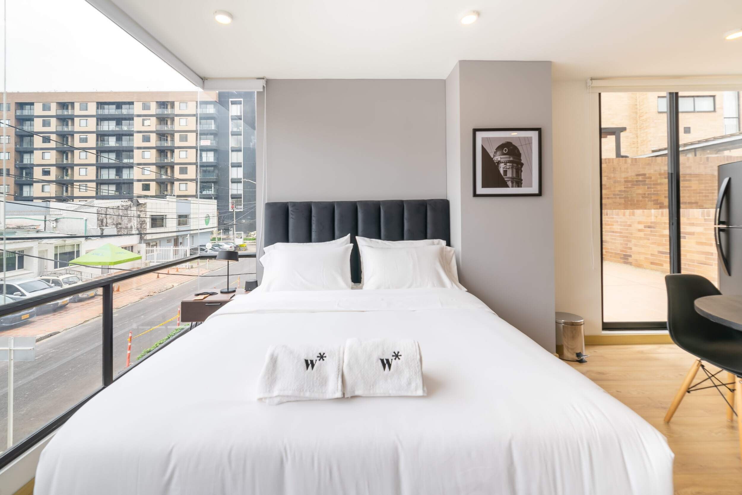Une chambre d’hôtel moderne avec un grand lit, une vue sur la ville et un balcon équipé d’une chaise.