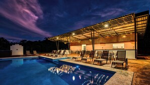 Una piscina con sillones de descanso y una zona de estar cubierta al anochecer.
