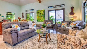 Amplia sala de estar con un juego de sofá gris, una mesa de centro de vidrio y un ventanal con vistas al exterior.