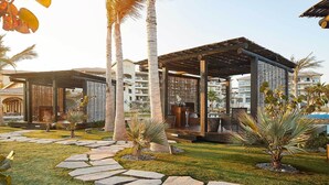 A courtyard with stone pathways, palm trees, and wooden pergolas.