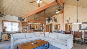 A spacious living room with a large sectional sofa, a wooden coffee table, and a dining area with wooden chairs and a chandelier. - Pagosa Springs Family Retreat w/ Game Room & Views (Pagosa Springs)