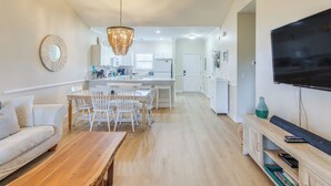 A modern kitchen with white cabinets, a dining area with a wooden table and chairs, and a living room with a sofa and a TV. - Resort Condo w/ Pool Access Near Barefoot Landing! (North Myrtle Beach)