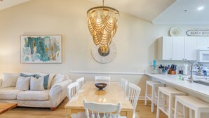 A modern kitchen with white cabinetry, a wooden dining table, and a hanging light fixture. - Resort Condo w/ Pool Access Near Barefoot Landing! (North Myrtle Beach)