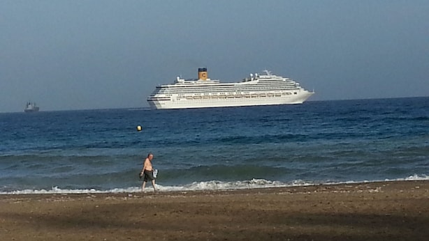 Un grand navire de croisière sur l’océan, avec une personne qui se promène sur la plage.