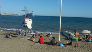 Une plage où l’on voit des gens se détendre, des parasols et un mât de drapeau.
