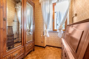 Une pièce comprenant une commode en bois, un miroir, un lit avec une tête de lit et une fenêtre avec des rideaux.