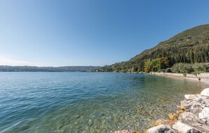 Un lac aux eaux limpides, bordé d’une rive rocheuse, avec une colline boisée en arrière-plan.