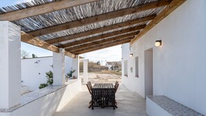 A covered patio area with a wooden table and chairs, white walls, and a view of the surrounding landscape. - Holiday Home 'Mas Midó' with Mountain View, Wi-Fi and Air Conditioning (Sant Jaume d'Enveja)