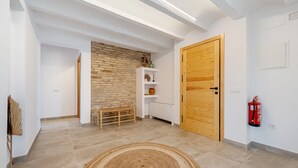 A hallway with a wooden door, a fire extinguisher, a bench, and a stone wall. - Holiday Home 'Mas Midó' with Mountain View, Wi-Fi and Air Conditioning (Sant Jaume d'Enveja)