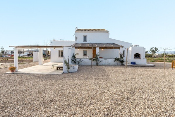 A white building with a tiled roof, a covered patio, and a gravel driveway.