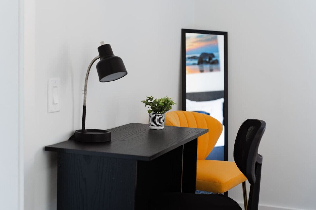 A desk with a black lamp, a small potted plant, and a framed picture on the wall.