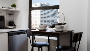 Eine moderne Küche mit Essbereich, Geschirrspüler, Kaffeemaschine und Blick auf eine Stadtlandschaft durch ein großes Fenster.