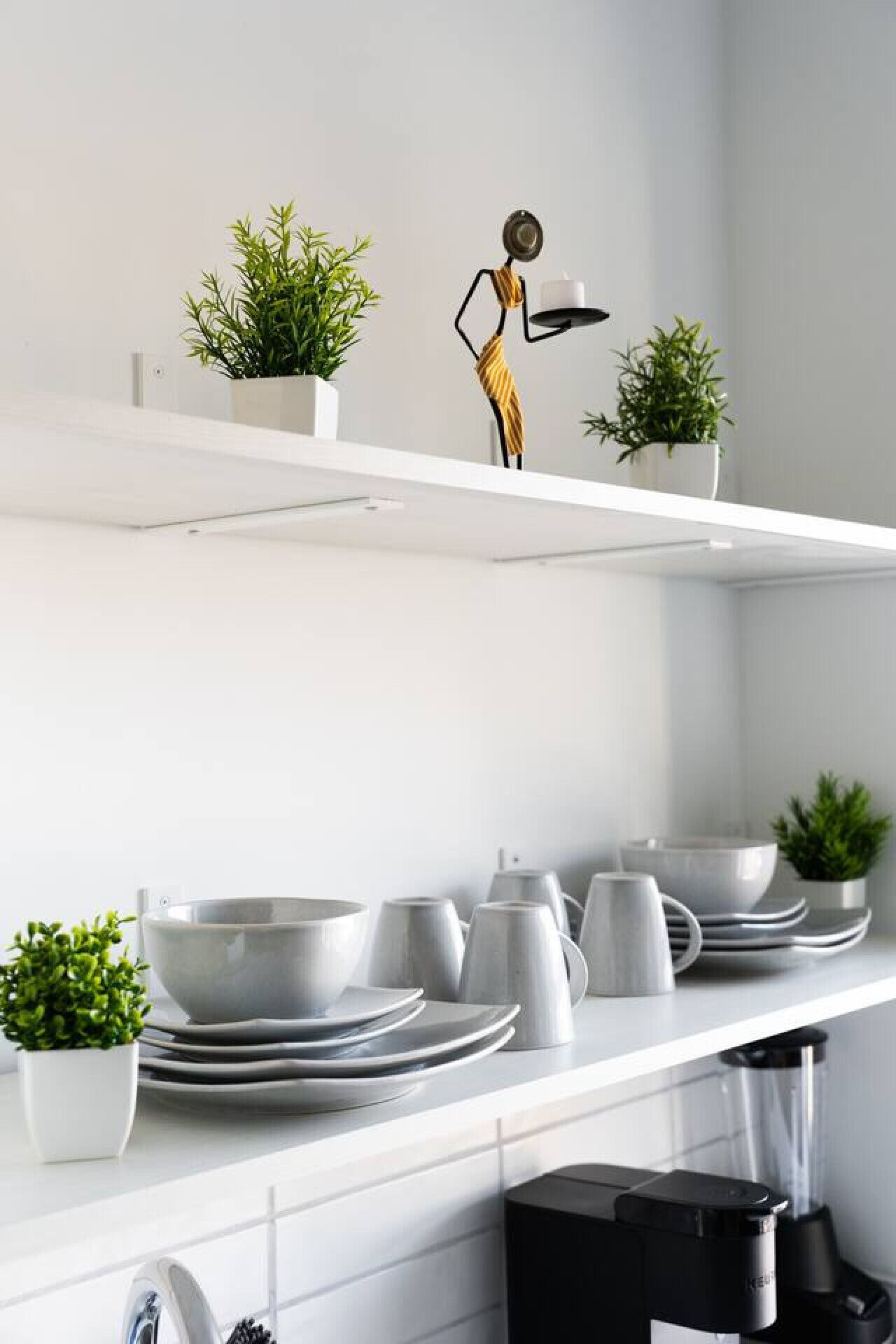 Een moderne keuken met witte planken, een decoratief beeldje en potplanten.