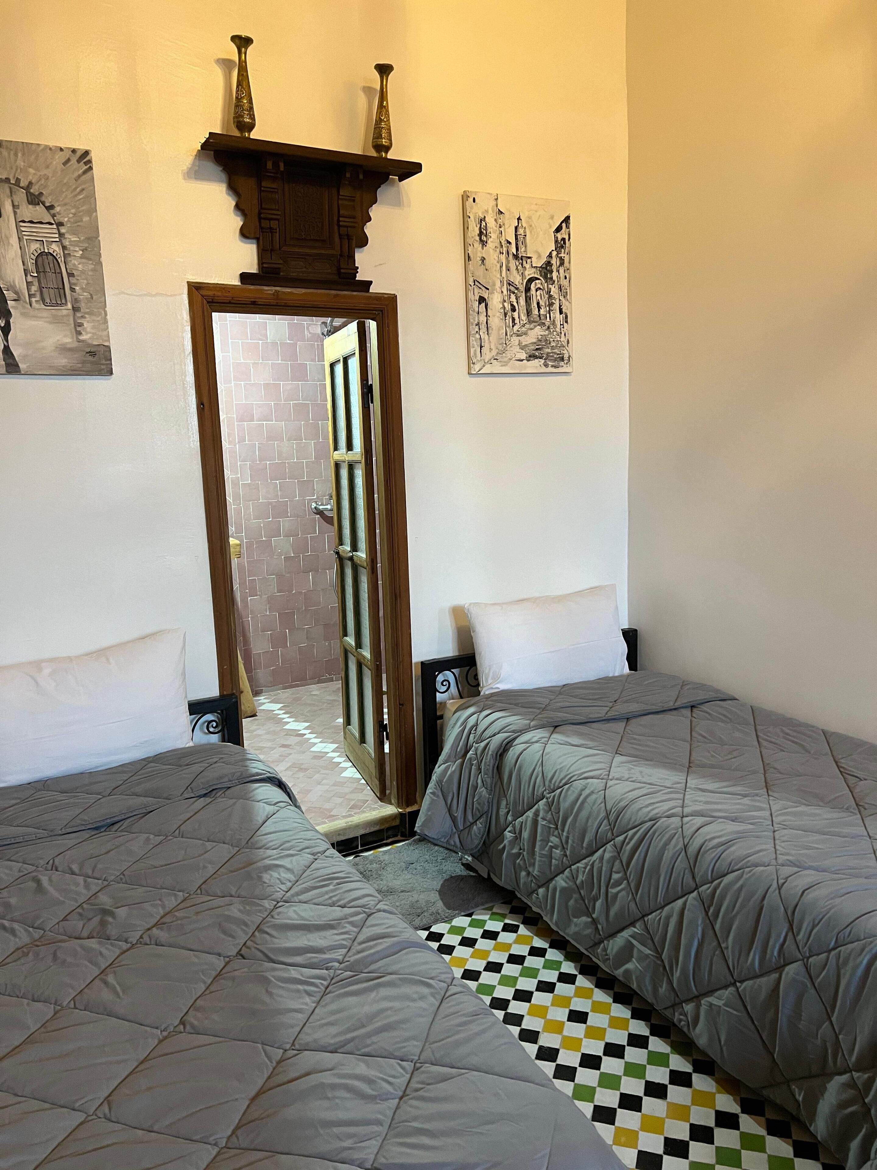 A room with two beds, a door leading to an outdoor area, and a wall with two artworks.
