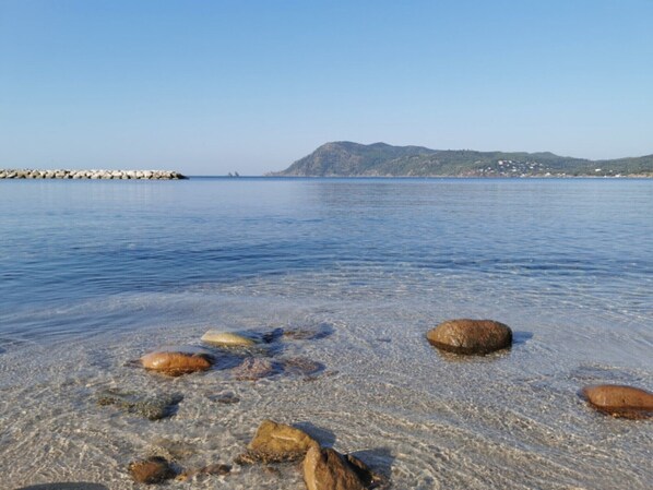 A calm sea with clear water, rocks on the shore, and distant mountains.