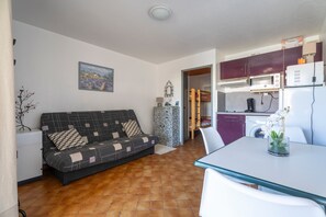 A compact living space with a sofa, a dining table, a kitchen area with a microwave, and a washing machine.