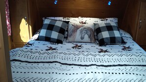 Un dormitorio de cabaña de madera con una cama, dos almohadas y una colcha estampada.