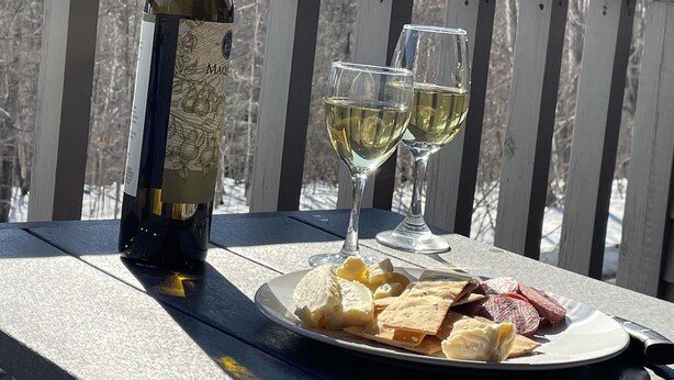 Una mesa de madera con una botella de vino, dos copas de vino blanco y un plato de aperitivos en un balcón.