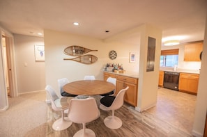 A modern kitchen with wooden cabinets, a dishwasher, and a dining area with a round table and white chairs.