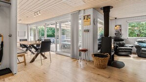 Ein modernes Wohnzimmer mit Holzboden, Kamin, Essbereich mit Tisch und Stühlen sowie einem großen Fenster mit Blick auf Grünflächen.