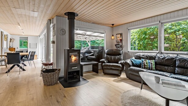 Ein modernes Wohnzimmer mit Kaminofen, Ledermöbeln und großen Fenstern mit Blick auf Grünflächen.