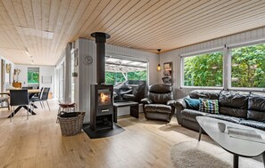 Cozy living space with a central stove, comfortable seating, and dining area, offering views of the surrounding greenery.