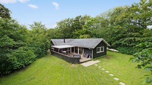 Eine kleine Hütte mit überdachter Terrasse und einer Holzterrasse, umgeben von üppigem Grün.