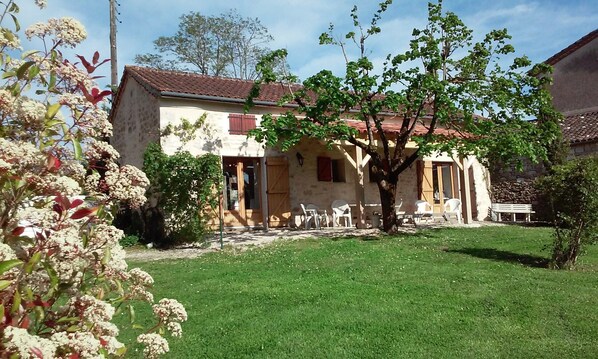 Una casa de piedra rústica con techo de tejas, un pequeño jardín con césped y mobiliario exterior.