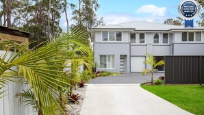 A modern two-story house with a grey exterior, white window shutters, and a driveway leading to the garage. - The Coast Beach - Pet Friendly - 2 Mins Walk to Bay (Callala Bay)