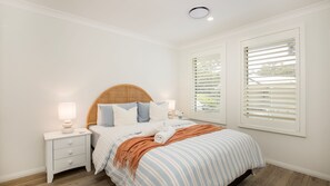A bedroom with a bed, nightstands, and a window with blinds.
