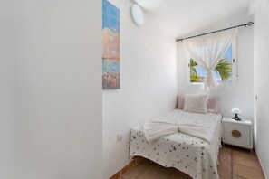 A bedroom with a bed, a nightstand, a window with curtains, a wall clock, and a painting.