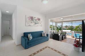 A living room with a blue sofa, a painting of a bicycle, and a view of a swimming pool.
