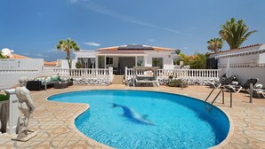 Ein Swimmingpool mit einem Sprungdolphin, umgeben von Liegestühlen und einer überdachten Terrasse.