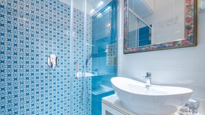 Une salle de bain avec un lavabo blanc, une cabine de douche en verre et des carreaux bleus à motifs.