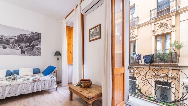 Une pièce avec un lit, une table sur laquelle se trouve un bol, un tableau encadré et un balcon agrémenté de plantes.