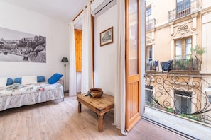 Quarto com cama, mesa com tigela, quadro emoldurado e varanda com plantas.