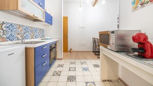 Une cuisine compacte avec des meubles bleus, un four à micro-ondes, une machine à café rouge et un pare-feu en carreaux.