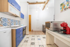 Une cuisine compacte avec des meubles bleus, un four à micro-ondes, une machine à café rouge et un pare-feu en carreaux.