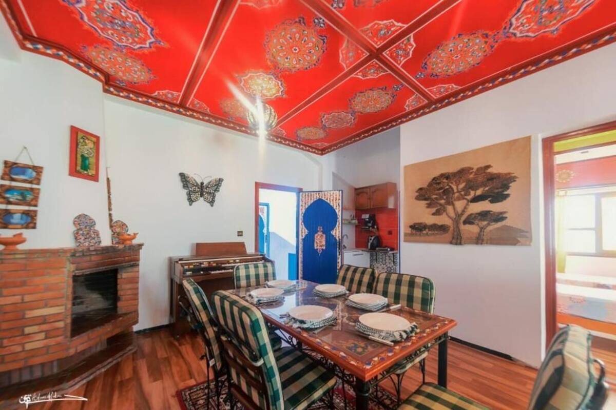 Ein Essbereich mit rot gemusterten Decken, einem Ziegelkamin und einem traditionellen Tisch, gedeckt für vier Personen.