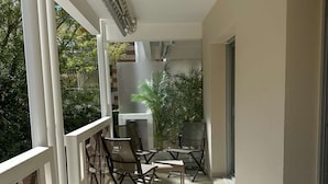 A balcony with a table and chairs, a potted plant, and a view of a building and trees.